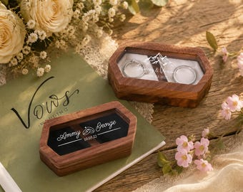 May include: Two hexagonal wooden ring boxes with clear lids. One box holds two silver rings and features a mountain graphic with the text Hailey & Patrick 09.23.2023. The other box has a black interior with the text Ammy & George 10.05.22.