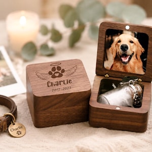 Pode incluir: Uma caixa quadrada de madeira escura com tampa articulada contendo a foto de um golden retriever. A tampa externa &eacute; gravada com uma pata, asas de anjo, uma aur&eacute;ola e o texto Charlie 2012-2023. Um pequeno frasco de vidro est&aacute; dentro da caixa.
