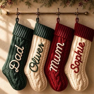 Può includere: Quattro calze natalizie in maglia appese a un'asta in ottone. La prima è verde scuro con la scritta bianca Dad, la seconda è color crema con la scritta verde scuro Oliver, la terza è rossa con la scritta bianca mum e la quarta è color crema con la scritta rossa Sophie.