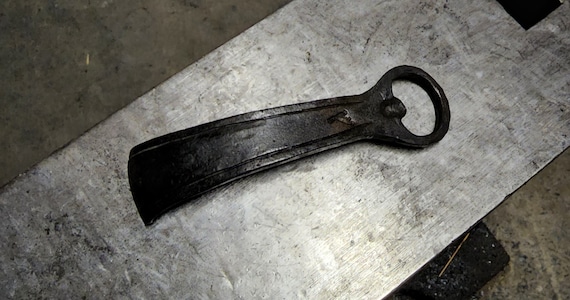 A hand-forged blacksmithed bottle opener — you can literally see the hammer marks, making it a functional keepsake that screams 'a real person made this at an anvil.'