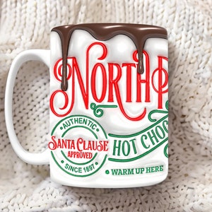 K&ouml;nnte beinhalten: Wei&szlig;e Keramiktasse mit einem roten und gr&uuml;nen Design, auf dem "North Pole Authentic Santa Clause Approved Since 1897 Warm Up Here" steht, mit einem schokoladenartigen &Uuml;berzug, der an der Seite heruntertropft.