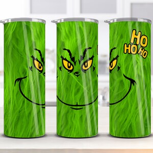 May include: Three green stainless steel tumblers with a Grinch face design. The middle tumbler has the Grinch's eyes and mouth, while the left and right tumblers show the Grinch's eyes and a green fuzzy texture. The right tumbler has the text "HO HO HO" in yellow.