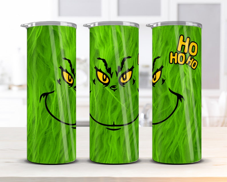 May include: Three green stainless steel tumblers with a Grinch face design. The middle tumbler has the Grinch's eyes and mouth, while the left and right tumblers show the Grinch's eyes and a green fuzzy texture. The right tumbler has the text "HO HO HO" in yellow.