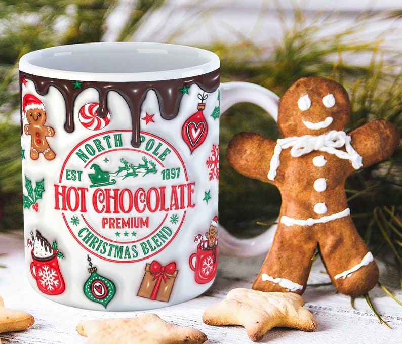 K&ouml;nnte beinhalten: Wei&szlig;e Keramiktasse mit einem roten, gr&uuml;nen und wei&szlig;en Weihnachtsmotiv. Die Tasse hat einen braunen Schokoladen-&auml;hnlichen &Uuml;berzug, der an der Seite heruntertropft. Die Tasse tr&auml;gt die Aufschrift "North Pole Est 1897 Hot Chocolate Premium Christmas Blend".