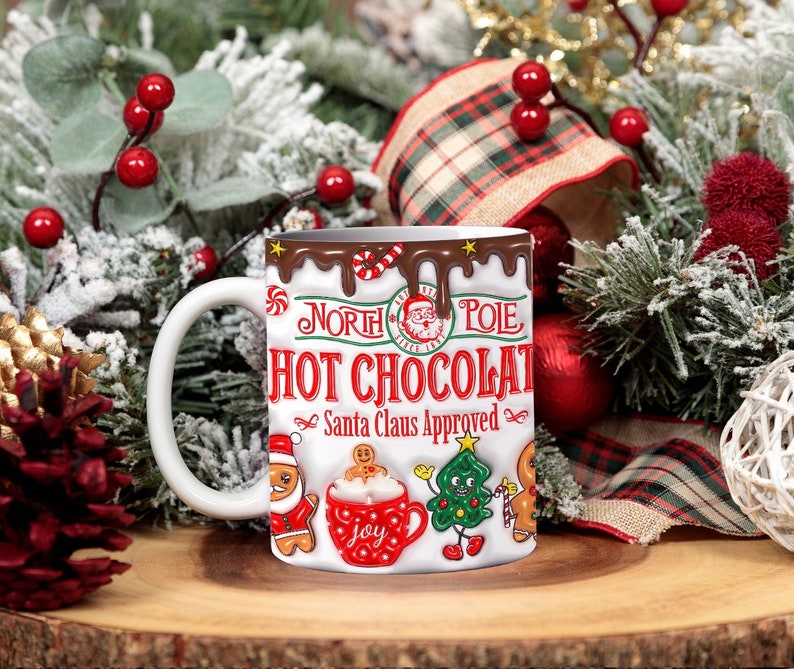 K&ouml;nnte beinhalten: Wei&szlig;e Keramiktasse mit einem rot-wei&szlig;-braunen Design. Die Tasse hat ein tropfendes Schokoladen-Design mit den Worten "Nordpol Hei&szlig;e Schokolade Vom Weihnachtsmann genehmigt" und einem Comic-Weihnachtsmann. Die Tasse ist von Weihnachtsdekoration umgeben.