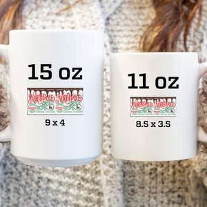 K&ouml;nnte beinhalten: Zwei wei&szlig;e Keramikbecher mit schwarzem Text und einer Grafik eines Nordpol-Hei&szlig;schokoladen-Etiketts. Der gr&ouml;&szlig;ere Becher ist 15 oz gro&szlig; und misst 9 x 4 Zoll. Der kleinere Becher ist 11 oz gro&szlig; und misst 8,5 x 3,5 Zoll.