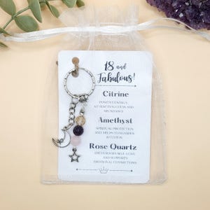 May include: A silver keychain with a charm featuring a crescent moon and star, along with Citrine, Amethyst, and Rose Quartz beads. The attached tag reads "18 and Fabulous!" with descriptions of the gemstones.