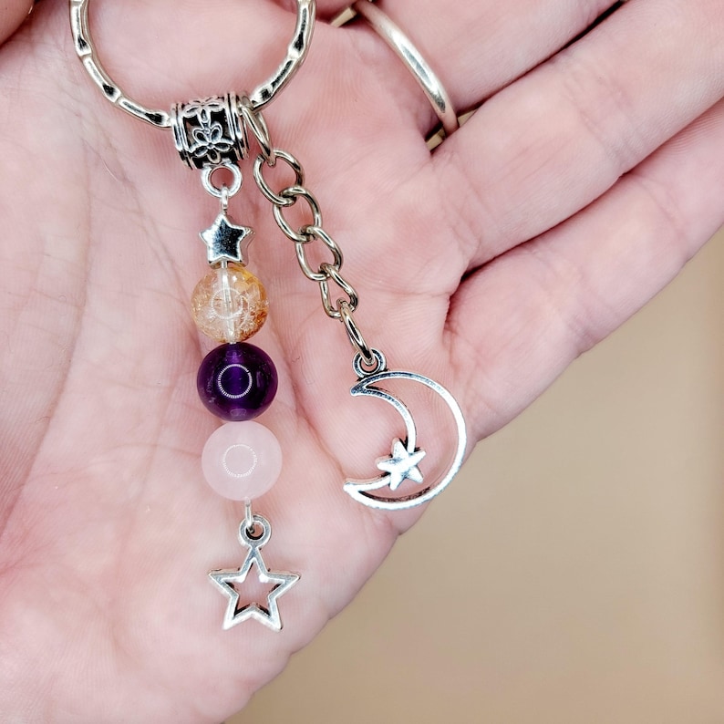 May include: A silver keychain with a decorative charm featuring a crescent moon and star, plus a chain of beads in shades of orange, purple, and pink. The keychain also has a star charm at the bottom.