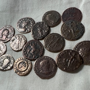 Peut inclure: Une collection de 14 pièces de monnaie argentées avec différents motifs et inscriptions. Les pièces sont disposées de manière aléatoire sur une surface en tissu blanc.