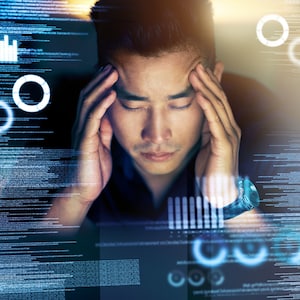 May include: A man with dark hair is sitting in front of a computer screen. He is holding his head in his hands, looking stressed. The screen shows lines of code and a few circles.