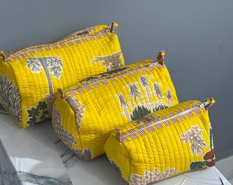 Pode incluir: Três sacos de tecido acolchoado amarelo com estampa botânica. Os sacos são cilíndricos com fecho de zíper e acabamento listrado. Os sacos são de tamanhos diferentes, o maior no topo.