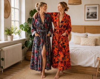 May include: Two long-length robes featuring floral patterns. One robe is a muted grey-blue with pink and red flowers, while the other is a vibrant orange with dark red and black floral motifs. Both robes have long sleeves, waist ties, and pockets.