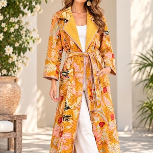 May include: A long, mustard yellow duster coat featuring a vibrant floral print in shades of pink, orange, and black. The garment has a wide lapel, long sleeves, two front pockets, and a matching fabric tie belt with a white and brown stitched trim.