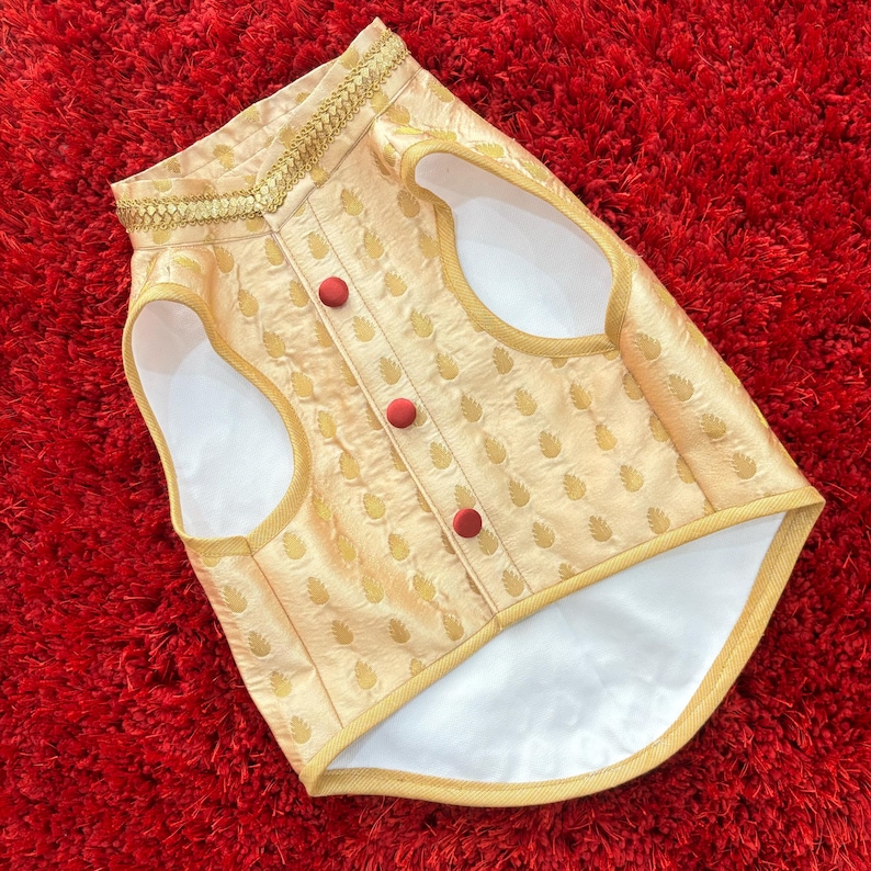 May include: A gold vest with a white lining and red buttons. The vest has a paisley pattern and a gold trim around the neckline.