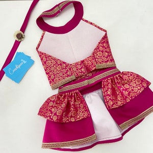 May include: A magenta dog outfit with gold floral brocade fabric and gold trim. The outfit includes a halter top, skirt, and matching leash with a decorative flower. The brand name "Coochipoo" is on a blue card.