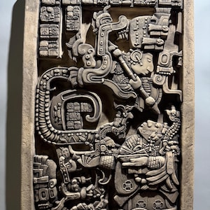 May include: A rectangular stone relief plaque featuring intricate bas-relief carvings of two figures in profile, surrounded by elaborate headdresses, ceremonial attire, and a border of Mayan glyphs. The sculpture has a matte, light gray finish.