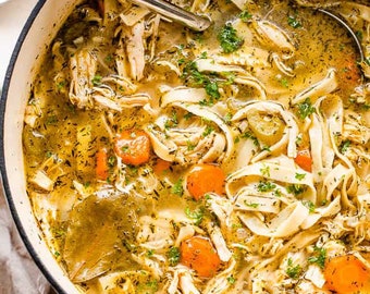 May include: A white pot filled with chicken noodle soup. The soup is topped with fresh parsley and carrots.