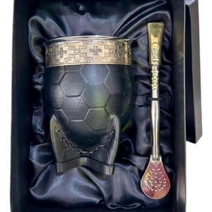 Peut inclure: Un récipient à maté en cuir noir avec un motif de ballon de football, un bord argenté avec un motif de croix et une paille bombilla en métal. L'ensemble est présenté dans un coffret cadeau noir avec une doublure en satin.