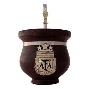 Puede incluir: Una calabaza de mate de madera marrón oscuro con una banda plateada y un emblema dorado con tres estrellas y las letras "AFA".