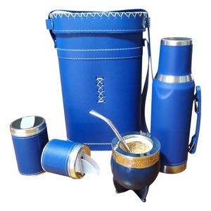 Puede incluir: Un juego de yerba mate azul que incluye un estuche alto, un termo, una calabaza con una pajita de metal y dos recipientes pequeños. El juego tiene detalles plateados y costuras blancas. La calabaza está llena de yerba mate.