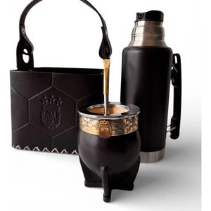 Puede incluir: Un juego de yerba mate negro con un estuche de cuero, un termo de acero inoxidable y una calabaza con una banda dorada. La calabaza tiene una pajita de metal. El juego está diseñado para disfrutar del yerba mate.
