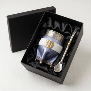 May include: A purple leather-wrapped mate gourd with a silver rim and base, featuring a white leather band with a gold-toned number 10 emblem. The set includes a long silver-toned metal bombilla with a perforated filter, presented in a black box.
