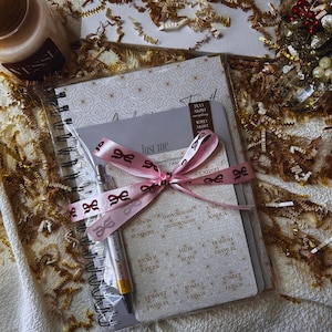 May include: A gift set including a spiral notebook, a small notepad, and a pen, all tied with a pink ribbon. The notepad features the text "Just me" and "beeseedStation BIBLE TABS". The set is packaged in clear plastic, with a decorative background.