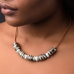 May include: A close-up of a brown leather cord necklace with white and brown striped ceramic beads.