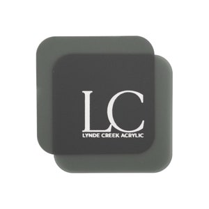 以下が含まれることがあります： 白い文字で「LC」と「Lynde Creek Acrylic」と書かれた灰色の正方形のアクリルコースター