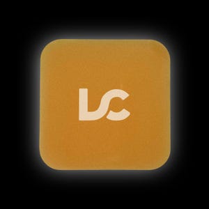Könnte beinhalten: Ein quadratisches, goldgelbes, schaumstoffartiges Pad mit den Buchstaben "LC" in Weiß in der Mitte.