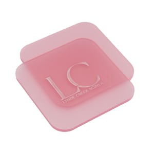 May include: Two square, pale pink acrylic coasters. The top coaster features the initials "LC" and the words "LYNDE CREEK ACRYLIC" etched in white. The coasters are slightly transparent with rounded corners.