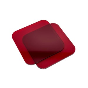 Può includere: Due sottobicchieri quadrati di colore rosso in vetro. I sottobicchieri sono impilati uno sopra l'altro.