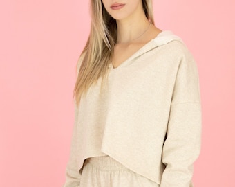 May include: A beige hooded sweatshirt and matching shorts set. The sweatshirt has a V-neck and a cropped hem. The shorts have an elastic waistband.