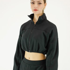 May include: A black cropped zip-up jacket with long sleeves and a matching black skirt with a red and blue stripe down the side.