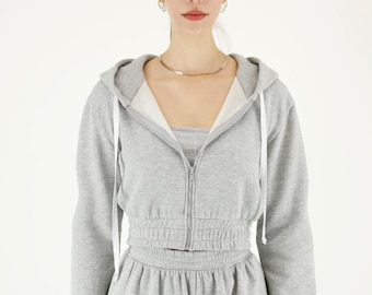 May include: A gray hooded sweatshirt with a zipper and a matching pair of sweatpants. The sweatshirt has a cinched waist and the sweatpants have a relaxed fit.
