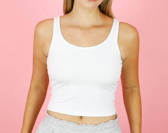May include: A white tank top with a scoop neck. The tank top is cropped and has a fitted silhouette.