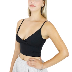 May include: A black, fitted, v-neck crop top with thin straps. The top is made of a soft, stretchy fabric and has a slightly relaxed fit. The model is wearing the top with grey sweatpants.