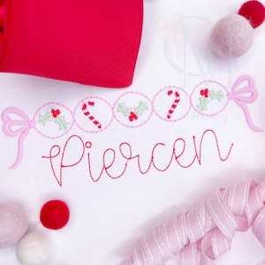 May include: A white embroidered design with a pink bow, candy canes, holly, and the name "Piersen" in red thread.