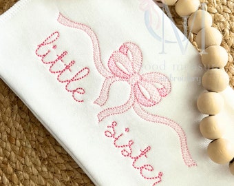 May include: White fabric with pink embroidery of a bow and the words "little sister".