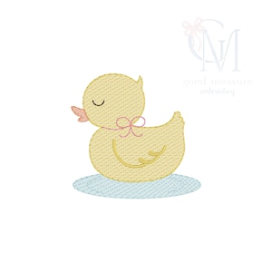 Puede incluir: Un pato amarillo bordado con un lazo rosa alrededor del cuello y una base azul claro. El pato tiene los ojos cerrados y un pequeño pico naranja. La imagen es un diseño de bordado digital.