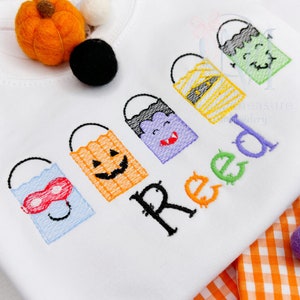 May include: White onesie with five embroidered trick-or-treat bags featuring different Halloween characters and the name "Reed" in black.