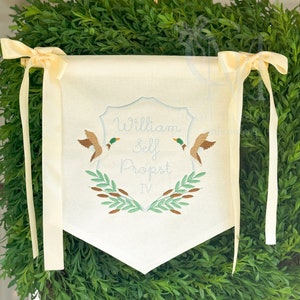 May include: A white banner with a blue and white embroidered crest featuring the name "William Self Probst IV" and two ducks. The banner has two white satin ribbons attached to the top.