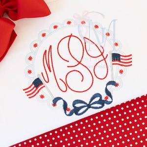 May include: White fabric with a red and blue embroidered design. The design features a monogram in red thread, surrounded by a scalloped edge and red star accents. Two small American flags and a blue ribbon complete the patriotic theme.