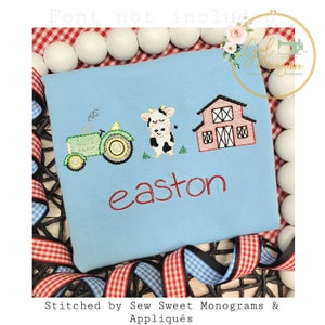 Peut inclure: Un t-shirt bleu clair avec des broderies sur le thème de la ferme : un tracteur vert, une vache noire et blanche et une grange rouge. Le nom "easton" est brodé en rouge. Le t-shirt est entouré de sphères blanches et de rubans rouges et bleus.