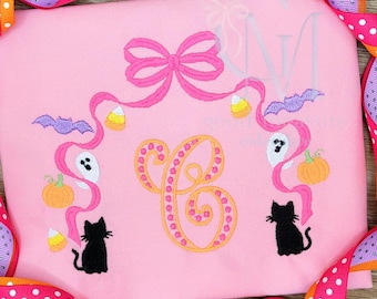 May include: Pink Halloween-themed shirt with a large orange and yellow letter "C" in the center. The shirt features embroidered Halloween elements, including a bow, bats, candy corn, ghosts, pumpkins, and black cats. A pink and orange polka dot ribbon frames the shirt.
