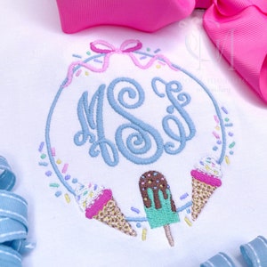 May include: A white embroidered design featuring a monogram "K.S.F." in blue surrounded by a wreath of pink and blue sprinkles and ice cream cones. The ice cream cones are decorated with pink, white, and yellow sprinkles. A green popsicle with chocolate drizzle is also included in the design.