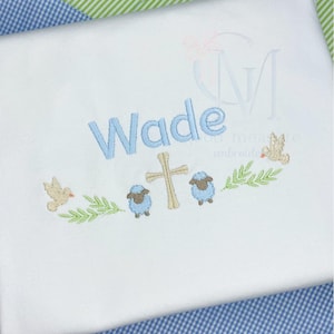 May include: White embroidered baby blanket with the name "Wade" in blue lettering, a cross, two lambs, a dove, and green leaves.