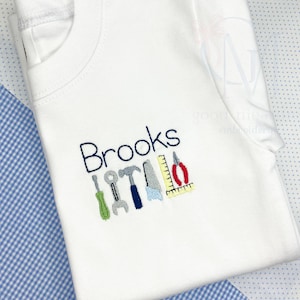 May include: White t-shirt with blue embroidery that says "Brooks" and a row of colorful tools underneath.