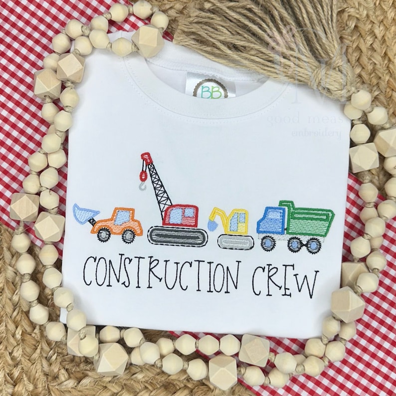 May include: White t-shirt with embroidered construction vehicles and the text "CONSTRUCTION CREW".