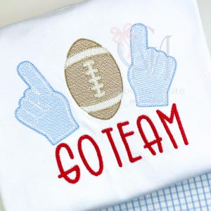 May include: White shirt with embroidered football, two foam fingers, and the words "GO TEAM" in red. The football is brown with white stitching, and the foam fingers are light blue.